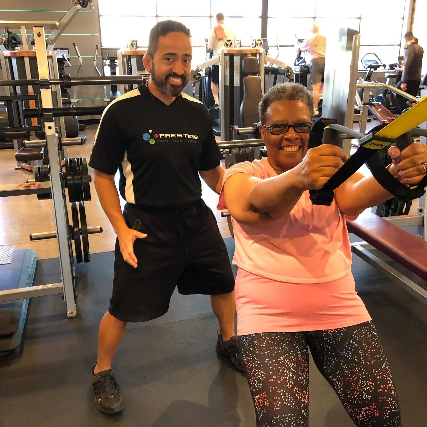 A Prestige Fitness coach and client smiling during a TRX session on the Tucson training floor