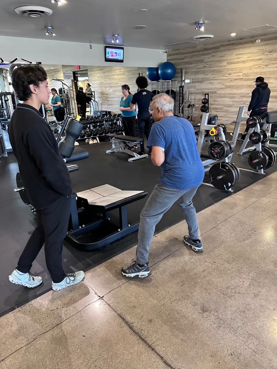 A Prestige Fitness coach spotting an adult client on the training floor in Tucson