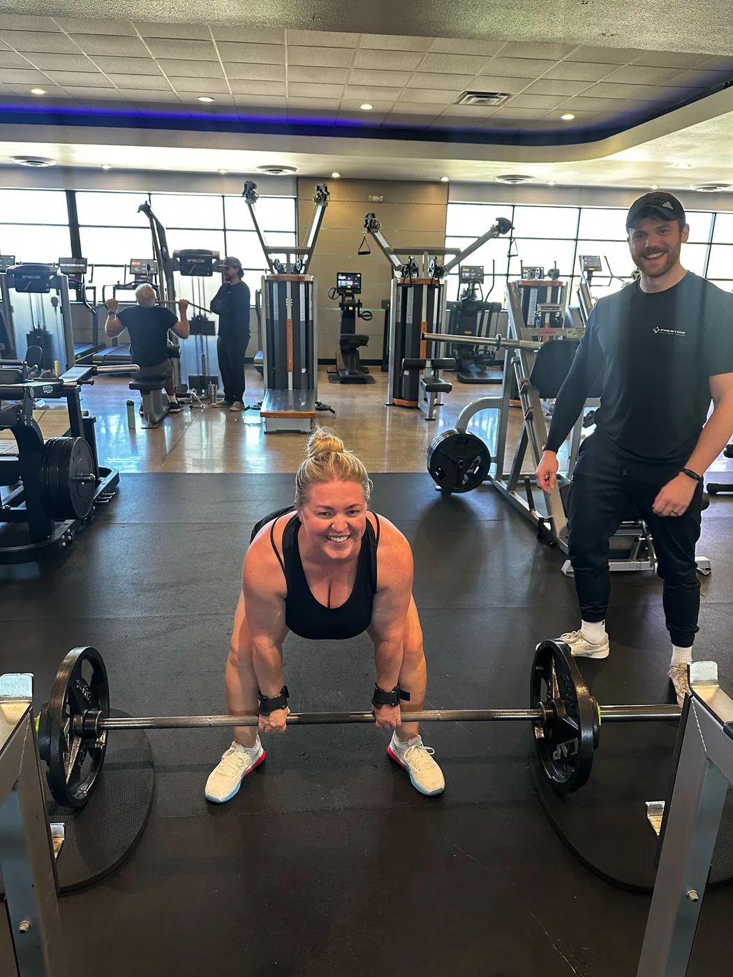 Prestige coach and client smiling during a sumo deadlift with the barbell visible