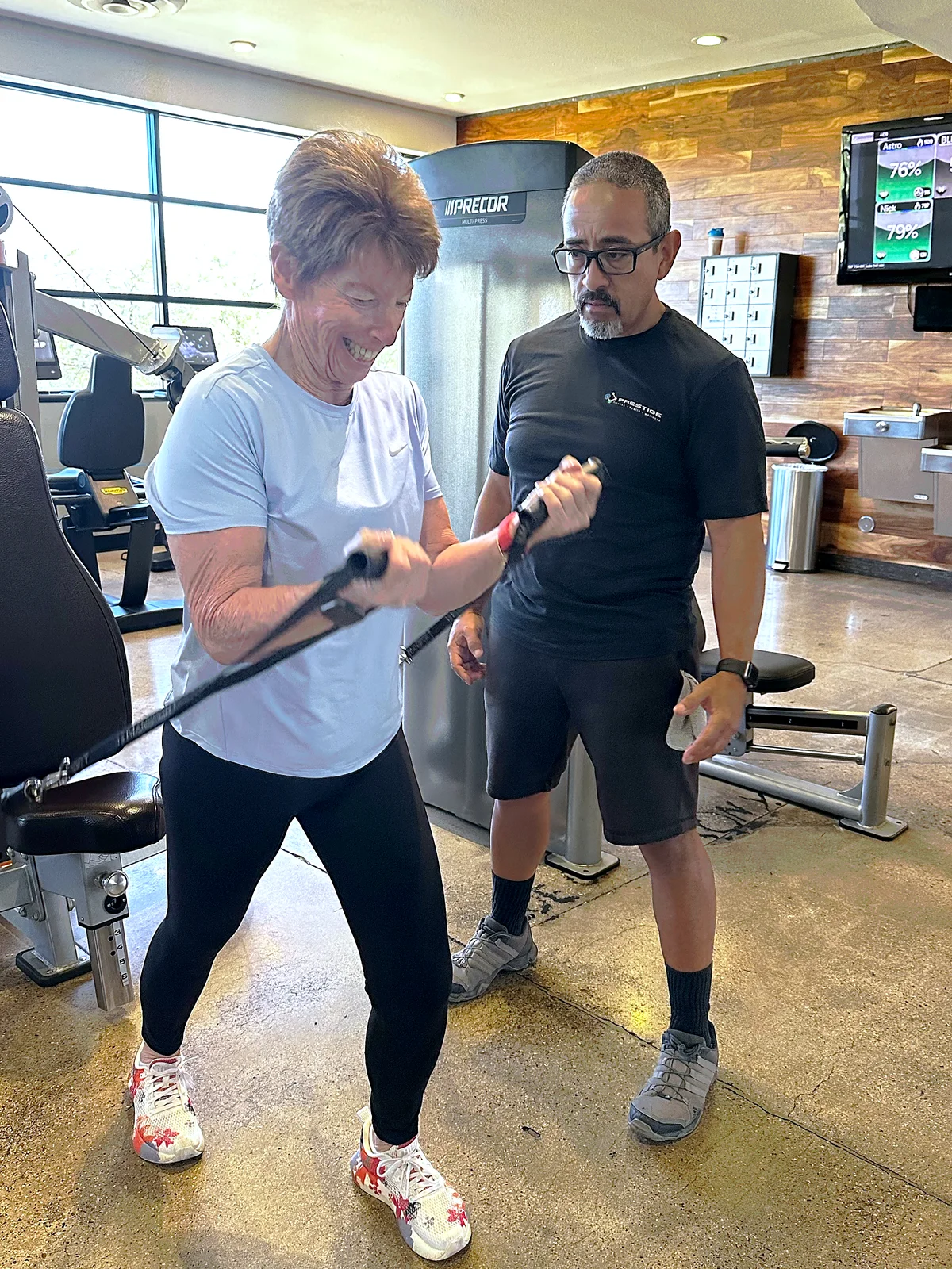 Prestige coach watching a laughing client during a cable curl in midtown Tucson