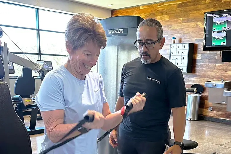 Prestige coach watching a laughing client during a cable curl in midtown Tucson