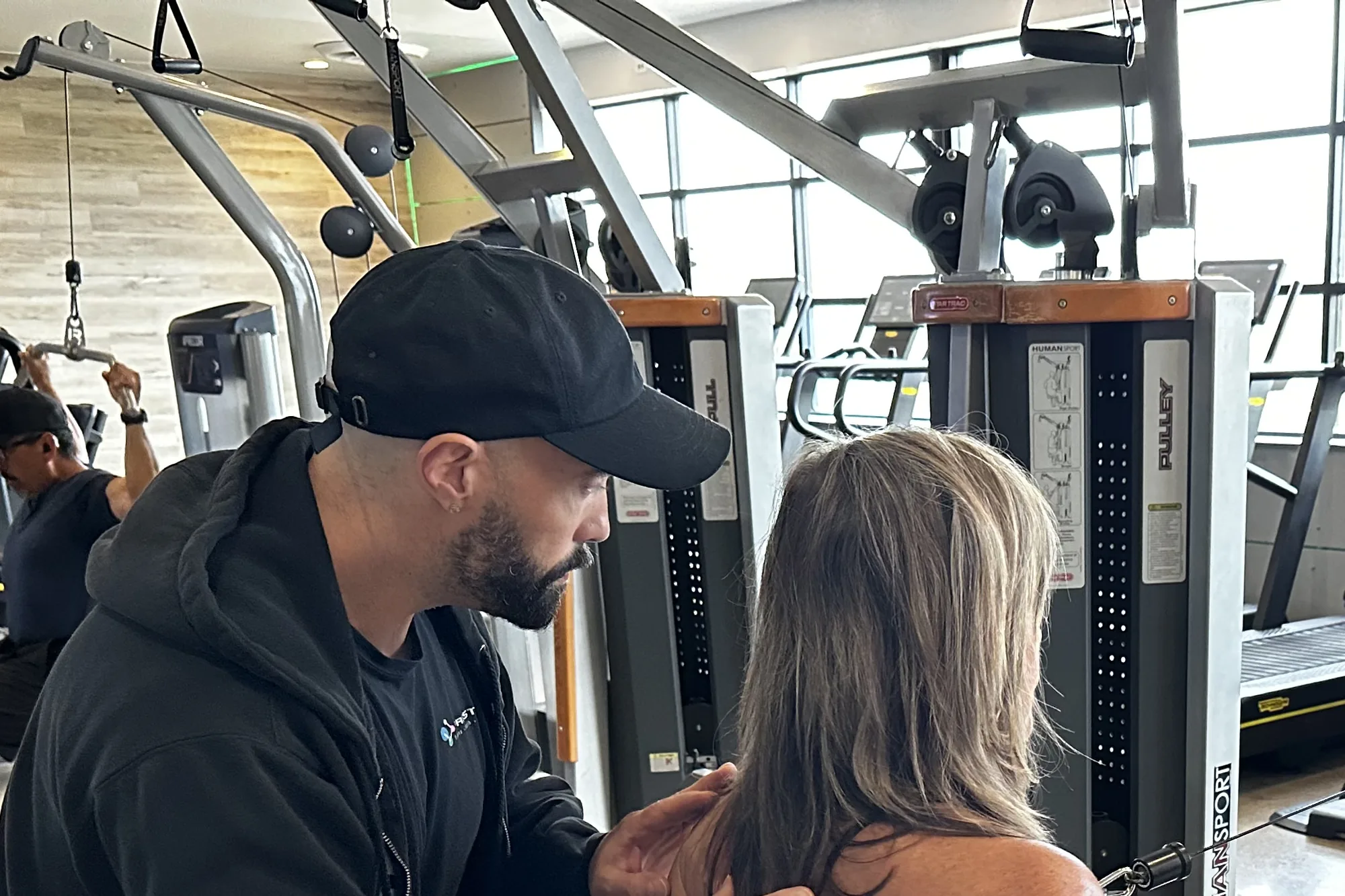 A Prestige coach hands-on cueing a client through a HumanSport cable strength movement